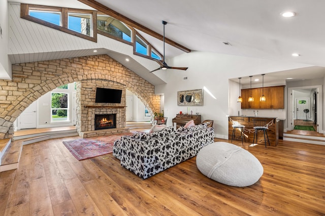 living room with hardwood / wood-style flooring, ceiling fan, a fireplace, and vaulted ceiling with beams