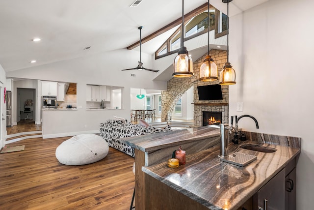 kitchen featuring white cabinets, a stone fireplace, beamed ceiling, sink, and stainless steel oven