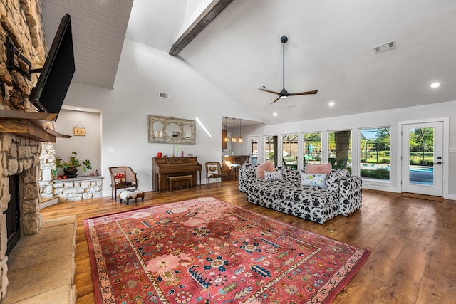 living room featuring beamed ceiling, a stone fireplace, ceiling fan, hardwood / wood-style flooring, and high vaulted ceiling