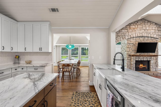 kitchen with white cabinetry, a fireplace, light stone countertops, stainless steel dishwasher, and sink