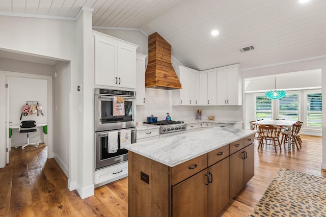 kitchen featuring white cabinets, appliances with stainless steel finishes, a kitchen island, light stone counters, and custom range hood