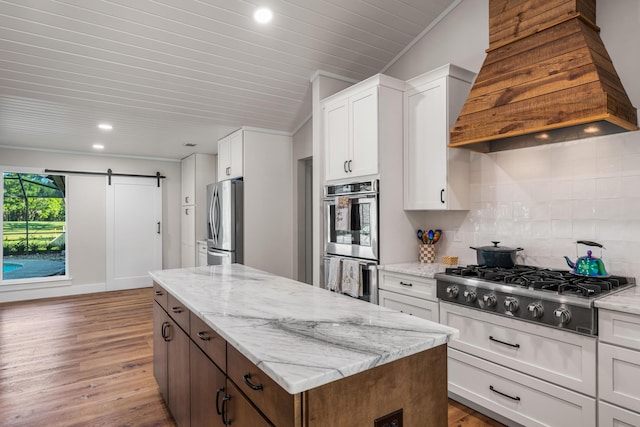 kitchen with stainless steel appliances, custom exhaust hood, a barn door, and white cabinetry