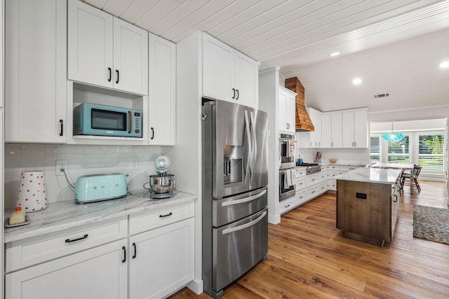 kitchen featuring tasteful backsplash, white cabinets, light stone counters, and stainless steel appliances