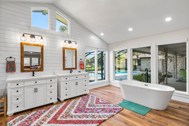 bathroom featuring vanity, hardwood / wood-style floors, a bath, wooden walls, and high vaulted ceiling