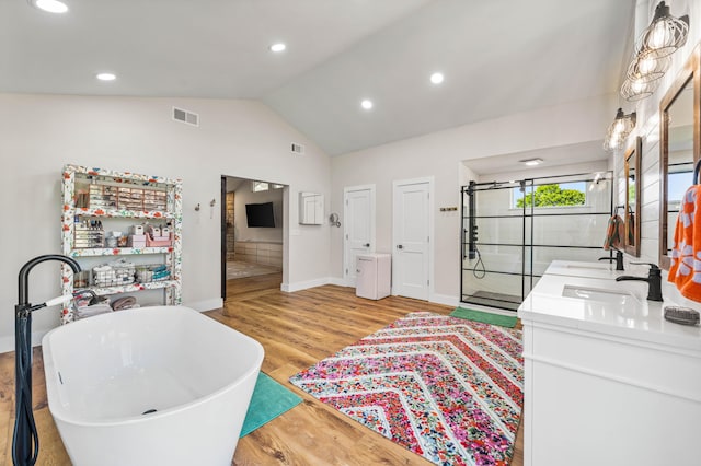 interior space featuring hardwood / wood-style flooring, a tub to relax in, vanity, and lofted ceiling