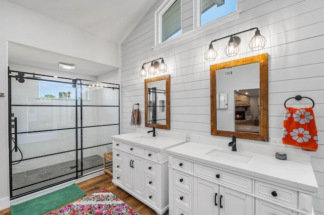 bathroom with walk in shower, vanity, vaulted ceiling, a fireplace, and hardwood / wood-style floors