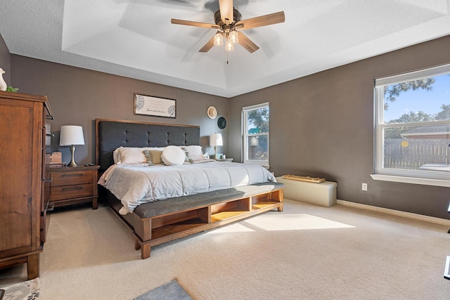 bedroom featuring light colored carpet, a raised ceiling, and ceiling fan