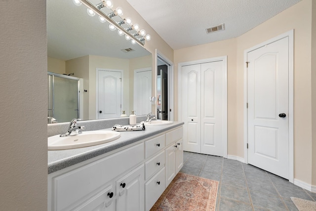 bathroom featuring tile patterned flooring, vanity, a shower with door, and a textured ceiling