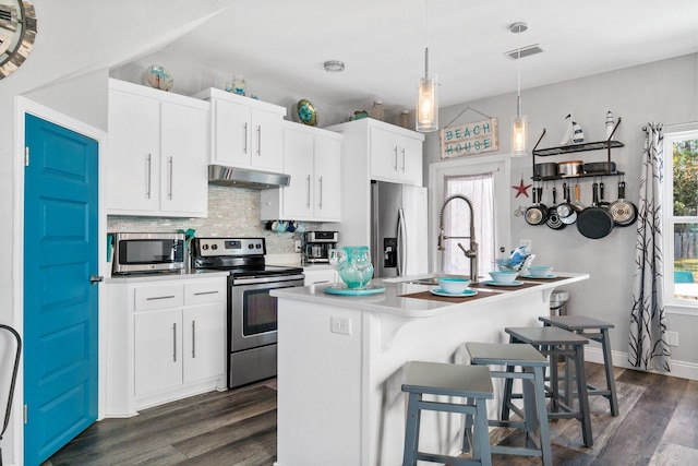 kitchen with hanging light fixtures, stainless steel appliances, range hood, a breakfast bar, and white cabinets