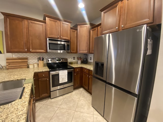 kitchen featuring sink, decorative backsplash, appliances with stainless steel finishes, light tile patterned flooring, and light stone counters