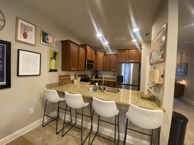 kitchen featuring a kitchen breakfast bar, light tile patterned flooring, light stone counters, kitchen peninsula, and stainless steel appliances