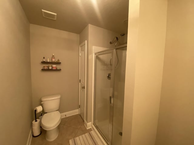 bathroom with tile patterned floors, a shower with door, and toilet