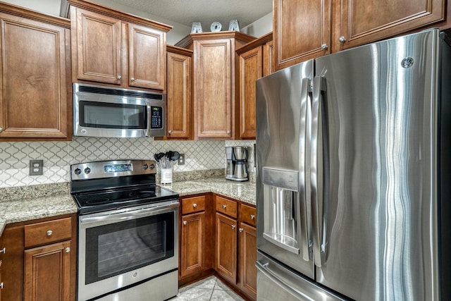 kitchen featuring light stone countertops, backsplash, a textured ceiling, light tile patterned flooring, and appliances with stainless steel finishes