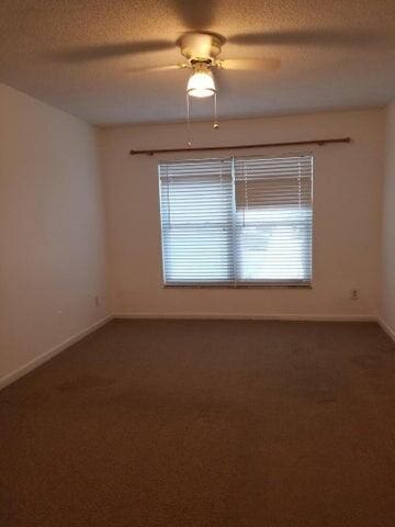 empty room featuring a wealth of natural light, ceiling fan, a textured ceiling, and dark colored carpet