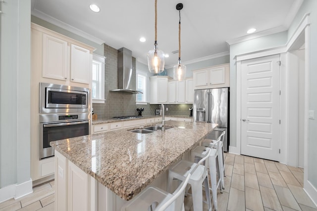 kitchen featuring pendant lighting, a center island with sink, wall chimney range hood, sink, and stainless steel appliances