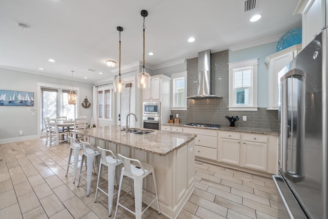 kitchen with stainless steel appliances, white cabinetry, a center island with sink, and wall chimney range hood