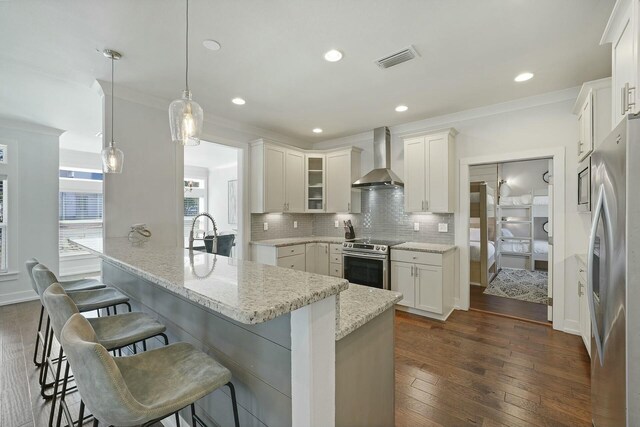 kitchen featuring pendant lighting, white cabinets, wall chimney range hood, appliances with stainless steel finishes, and dark hardwood / wood-style flooring