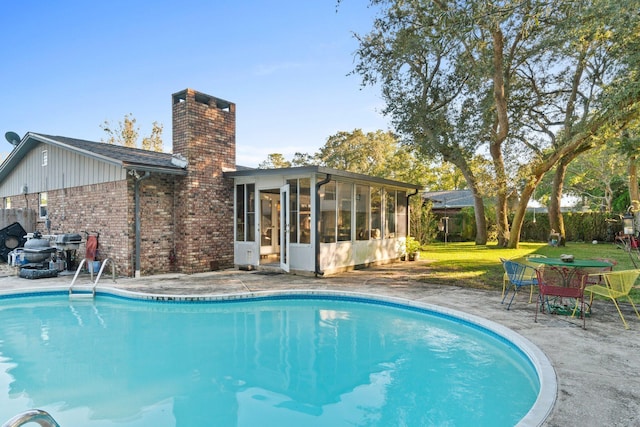 view of swimming pool with a sunroom, a patio area, and a yard