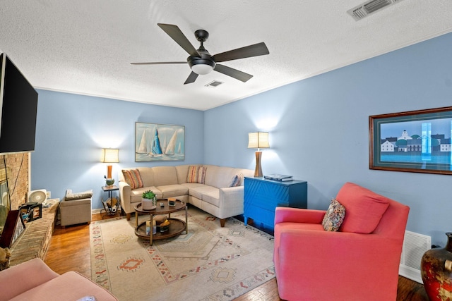 living room featuring ceiling fan, light wood-type flooring, a textured ceiling, and a brick fireplace