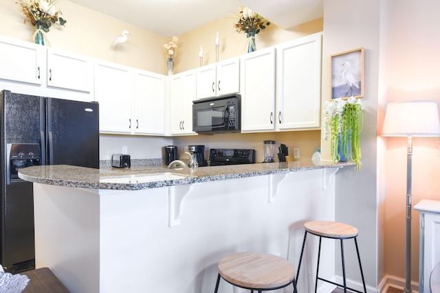 kitchen with kitchen peninsula, a kitchen breakfast bar, light stone countertops, black appliances, and white cabinets