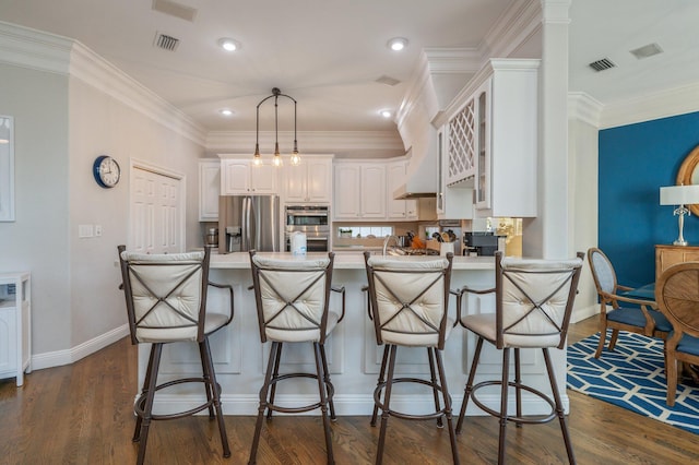 kitchen with pendant lighting, white cabinets, appliances with stainless steel finishes, kitchen peninsula, and a breakfast bar area