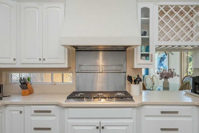 kitchen with stainless steel gas cooktop, decorative backsplash, white cabinetry, and custom exhaust hood