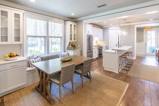 dining space with hardwood / wood-style floors, breakfast area, ornamental molding, and sink