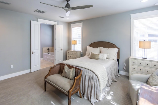 carpeted bedroom with ceiling fan, ensuite bathroom, and multiple windows