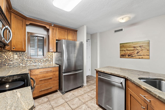 kitchen with light stone countertops, a textured ceiling, appliances with stainless steel finishes, tasteful backsplash, and light tile patterned flooring