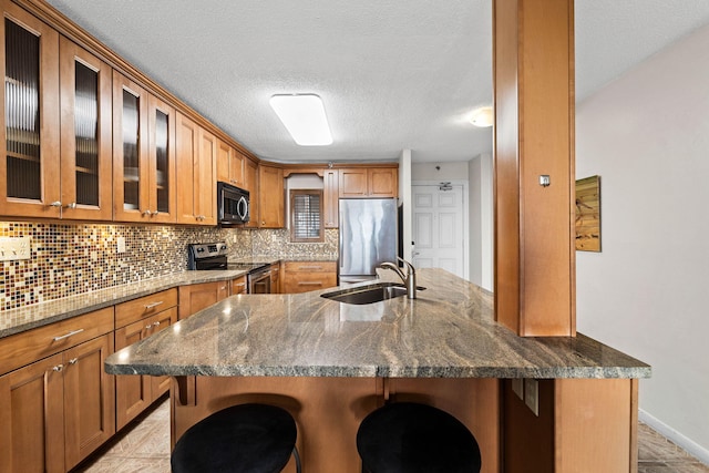 kitchen with appliances with stainless steel finishes, dark stone counters, a kitchen breakfast bar, and sink