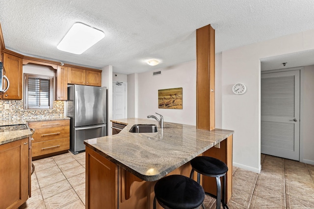 kitchen with a kitchen bar, a textured ceiling, stainless steel appliances, sink, and a kitchen island