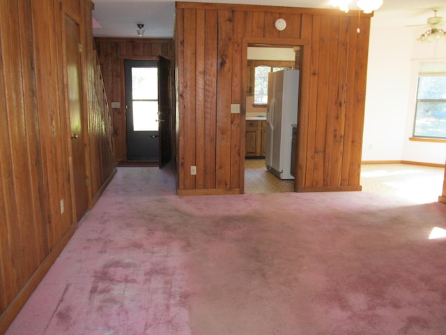 carpeted spare room featuring ceiling fan, wood walls, and a wealth of natural light