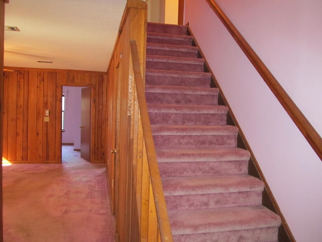 stairs with carpet flooring, wood walls, and vaulted ceiling