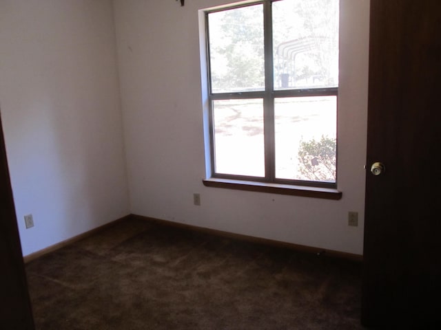 empty room with dark colored carpet and a wealth of natural light