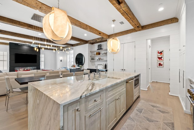 kitchen with a center island with sink, sink, light stone countertops, decorative light fixtures, and beam ceiling