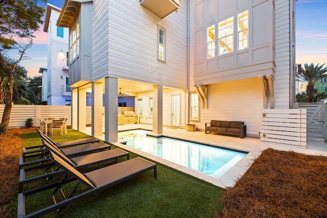 back house at dusk featuring an outdoor kitchen, a fenced in pool, and a patio