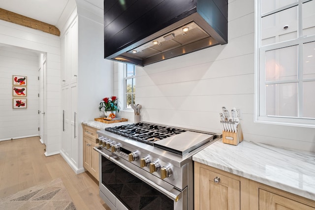 kitchen with premium range hood, wooden walls, high end stove, light brown cabinetry, and light hardwood / wood-style floors