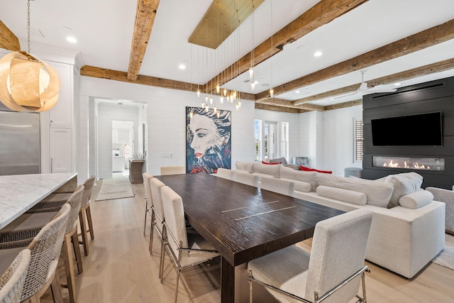 dining space with beamed ceiling, light hardwood / wood-style floors, and a large fireplace