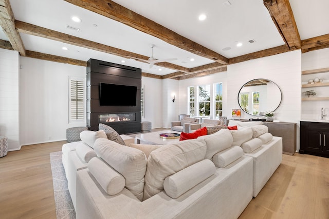 living room with ceiling fan, beam ceiling, light wood-type flooring, and a fireplace