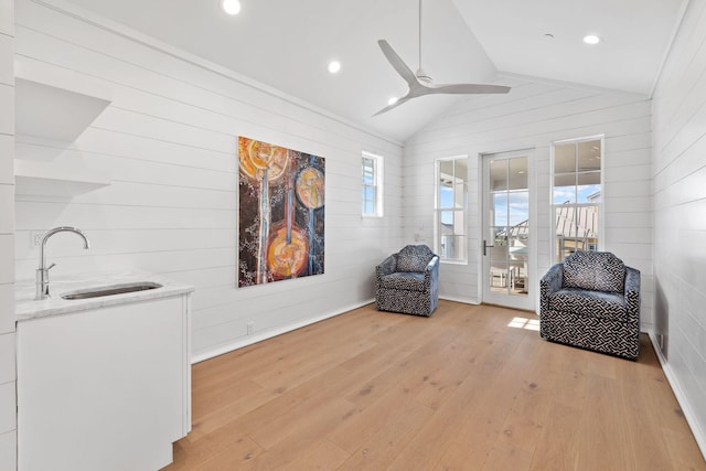 living area featuring wood walls, sink, lofted ceiling, and light wood-type flooring