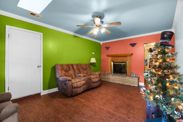 living room featuring a skylight, ornamental molding, ceiling fan, dark wood-type flooring, and a fireplace