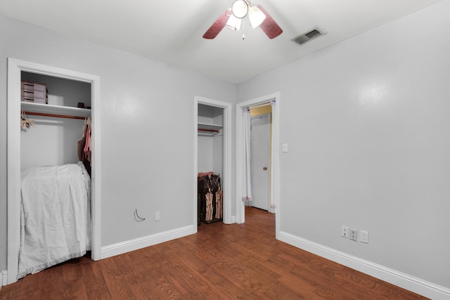 unfurnished bedroom featuring multiple closets, ceiling fan, and dark hardwood / wood-style flooring