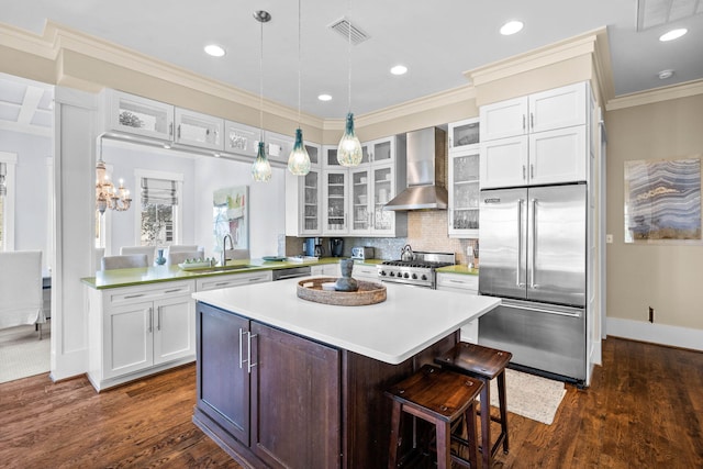 kitchen featuring wall chimney exhaust hood, premium appliances, kitchen peninsula, a kitchen bar, and white cabinets