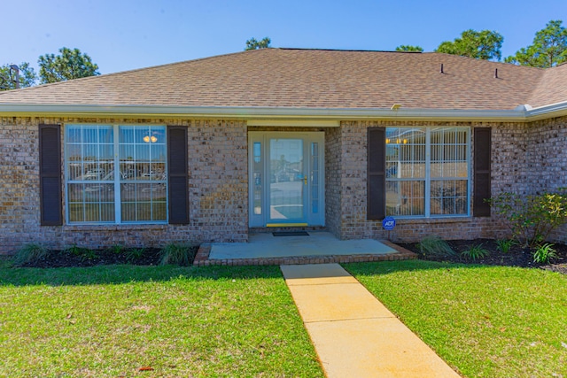 doorway to property with a lawn, brick siding, and a shingled roof