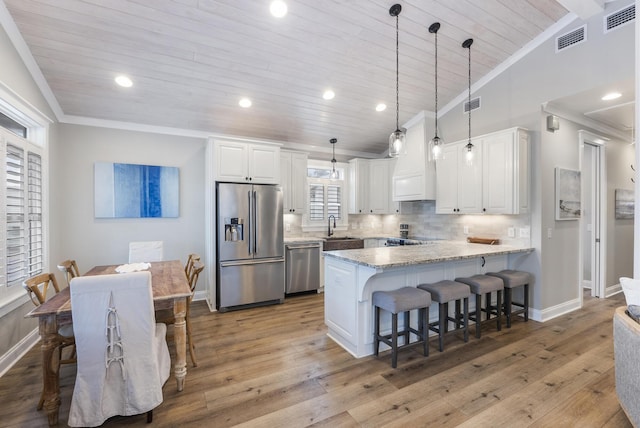 kitchen featuring white cabinets, appliances with stainless steel finishes, vaulted ceiling, and light stone counters