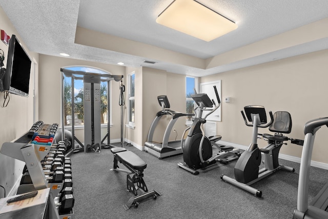 gym featuring a textured ceiling, a wealth of natural light, and a tray ceiling