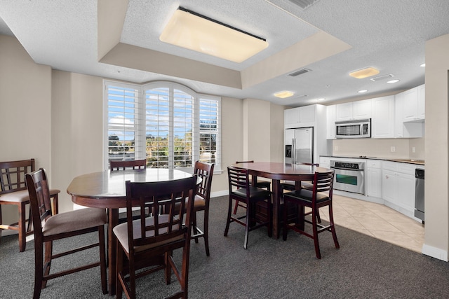 dining space featuring a tray ceiling, light tile patterned flooring, and a textured ceiling