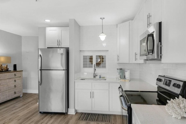 kitchen featuring white cabinets, sink, light hardwood / wood-style flooring, appliances with stainless steel finishes, and decorative light fixtures