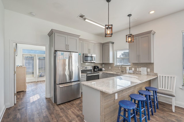 kitchen with pendant lighting, sink, appliances with stainless steel finishes, kitchen peninsula, and a breakfast bar area