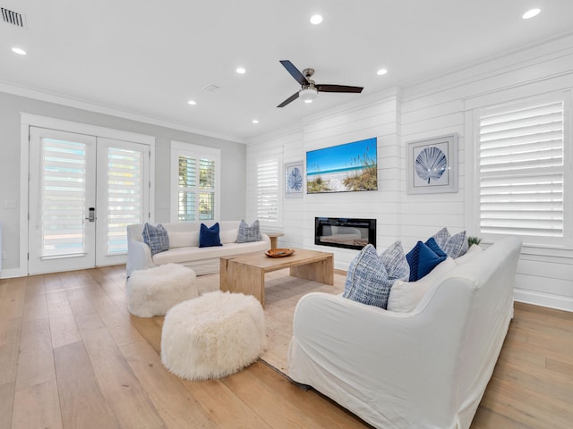 living room featuring french doors, ceiling fan, crown molding, a fireplace, and light hardwood / wood-style floors